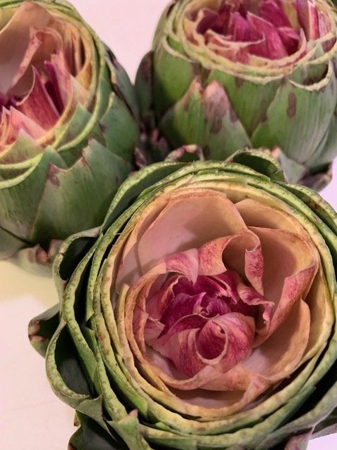 Three artichokes with purple flowers in them are sitting on a table.