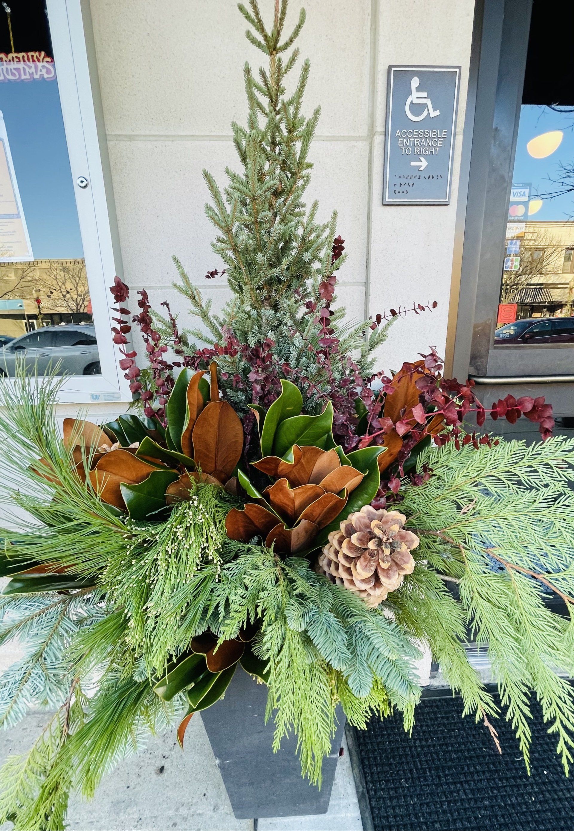 A potted plant with flowers and a christmas tree in front of a building.