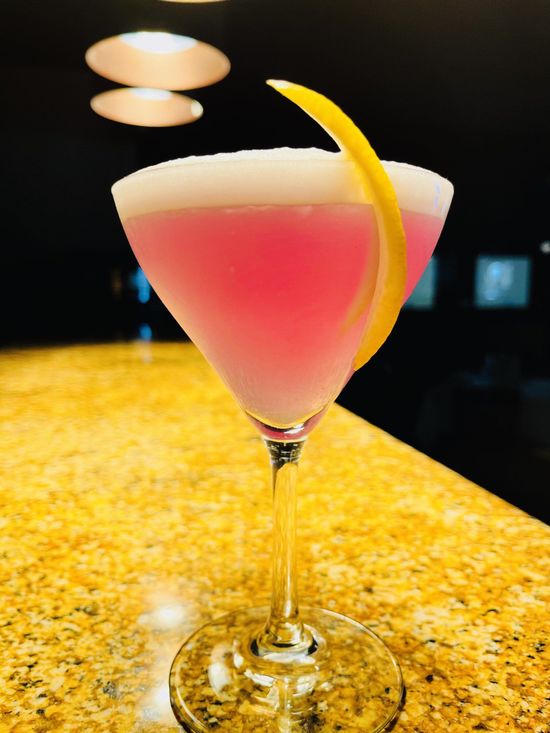 A pink cocktail in a martini glass on a bar