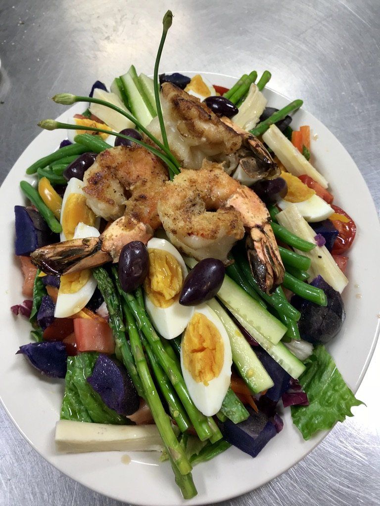 A salad with shrimp asparagus eggs and olives on a plate