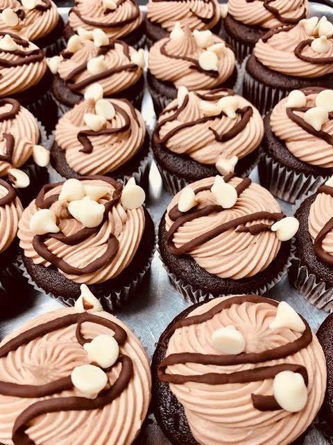 A tray of chocolate cupcakes with chocolate frosting and white chocolate chips.
