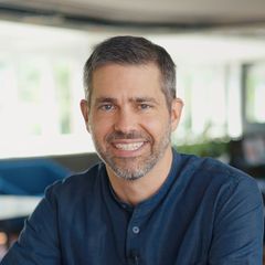 A man with a beard is smiling for the camera while wearing a blue shirt.