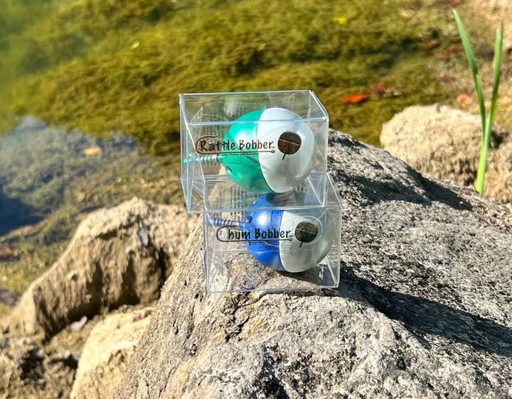 Two balls are sitting on top of a rock next to a body of water.