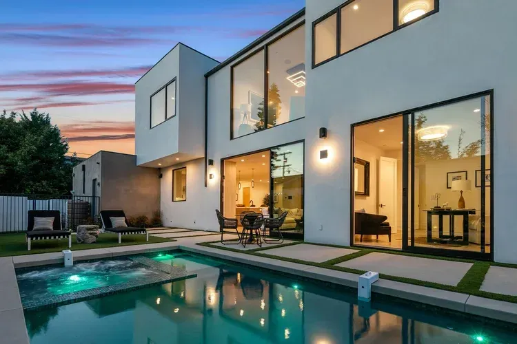 Modern two-story house with lit windows and a backyard pool at dusk