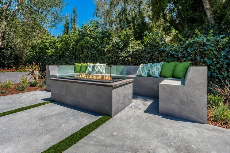 Modern outdoor patio with gray sectional seating, green cushions, and a fire table in a landscaped garden