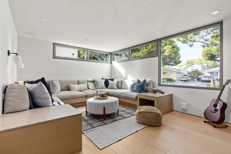 Bright modern living room with sectional sofa, round ottoman, large windows, and a guitar in the corner