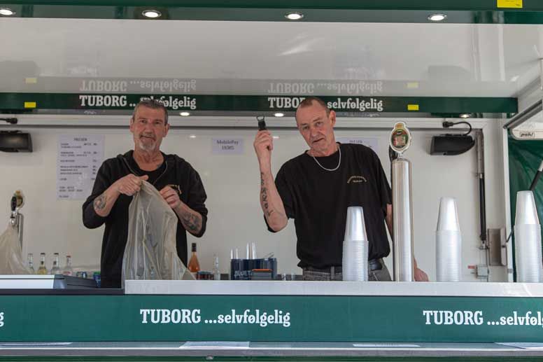 To mænd bag en bar, den ene holder en taske, den anden med en kniv, Tuborg-skilt.