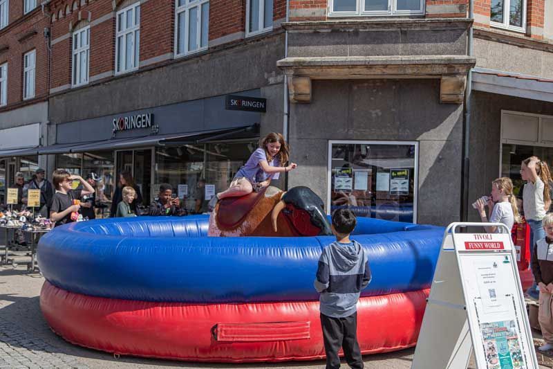 Pige rider på en mekanisk tyr i en blå og rød oppustelig ring på en bygade.