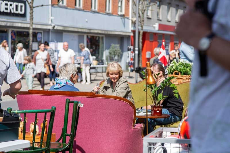 Folk på et udendørs marked; en lyserød sofa og vintagemøbler er til salg.