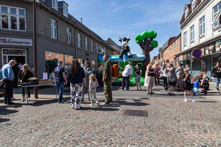 Folk samledes på en brostensbelagt gade med en oppustelig legestruktur med koer; butikker i baggrunden.