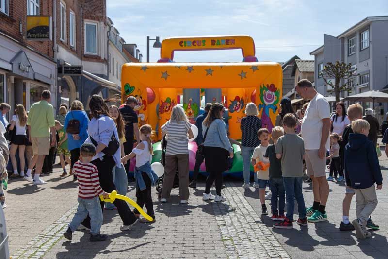 Folk samles på en murstensgade med en hoppeborg; en festlig udendørsbegivenhed.