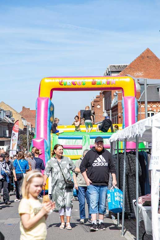 Folk går forbi en oppustelig forhindringsbane på en gade under et marked. Lys solskinsdag.