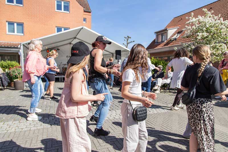 Folk danser udenfor under et telt på en solskinsdag.