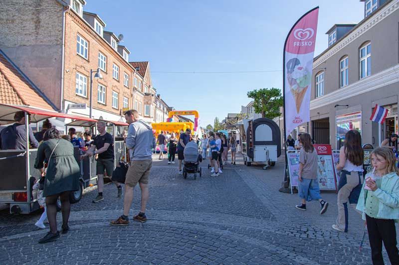Gademarked med mennesker, madboder og butikker på en solskinsdag.