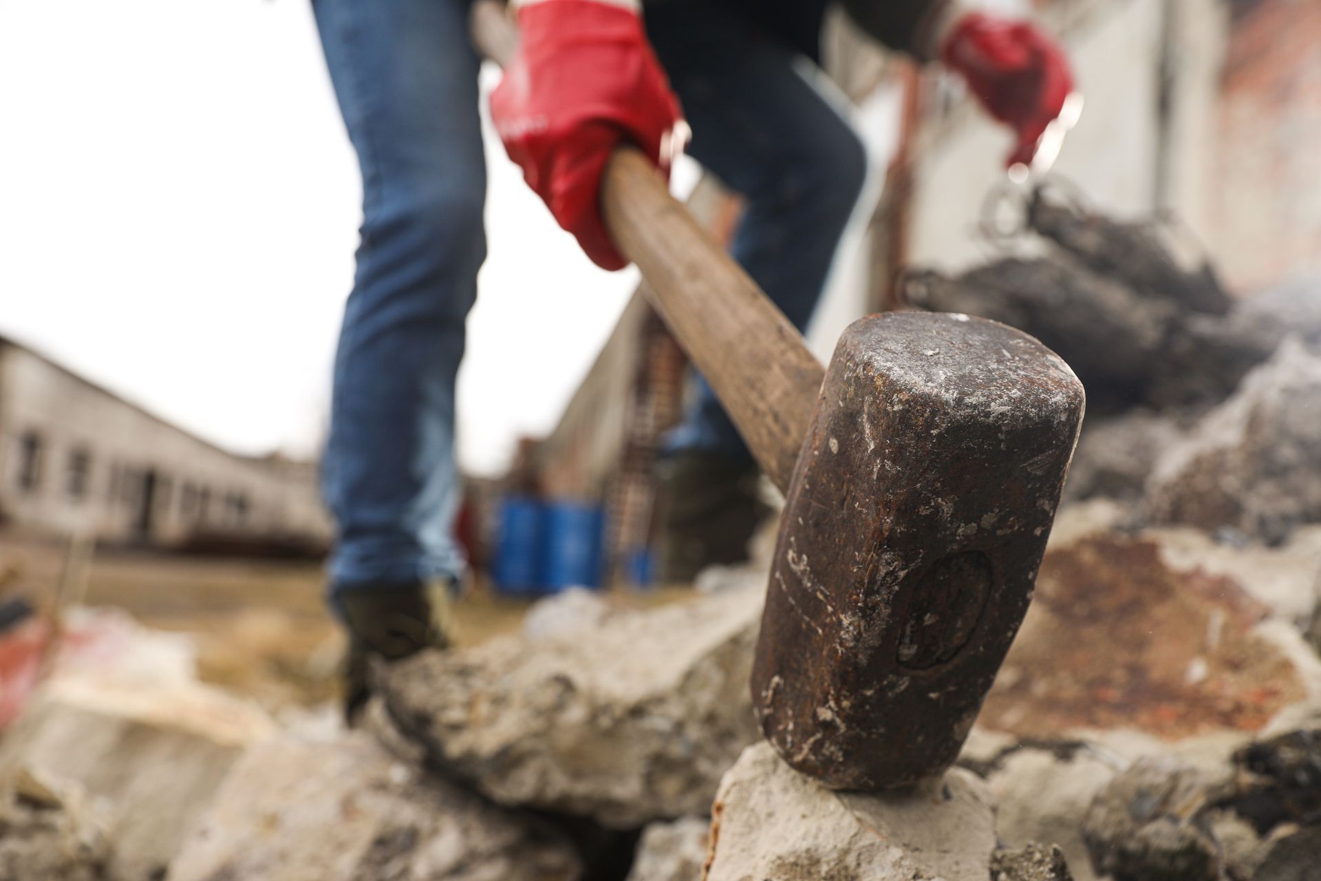 Two demolition workers breaking stones with sledgehammers outdoors with residences in the background