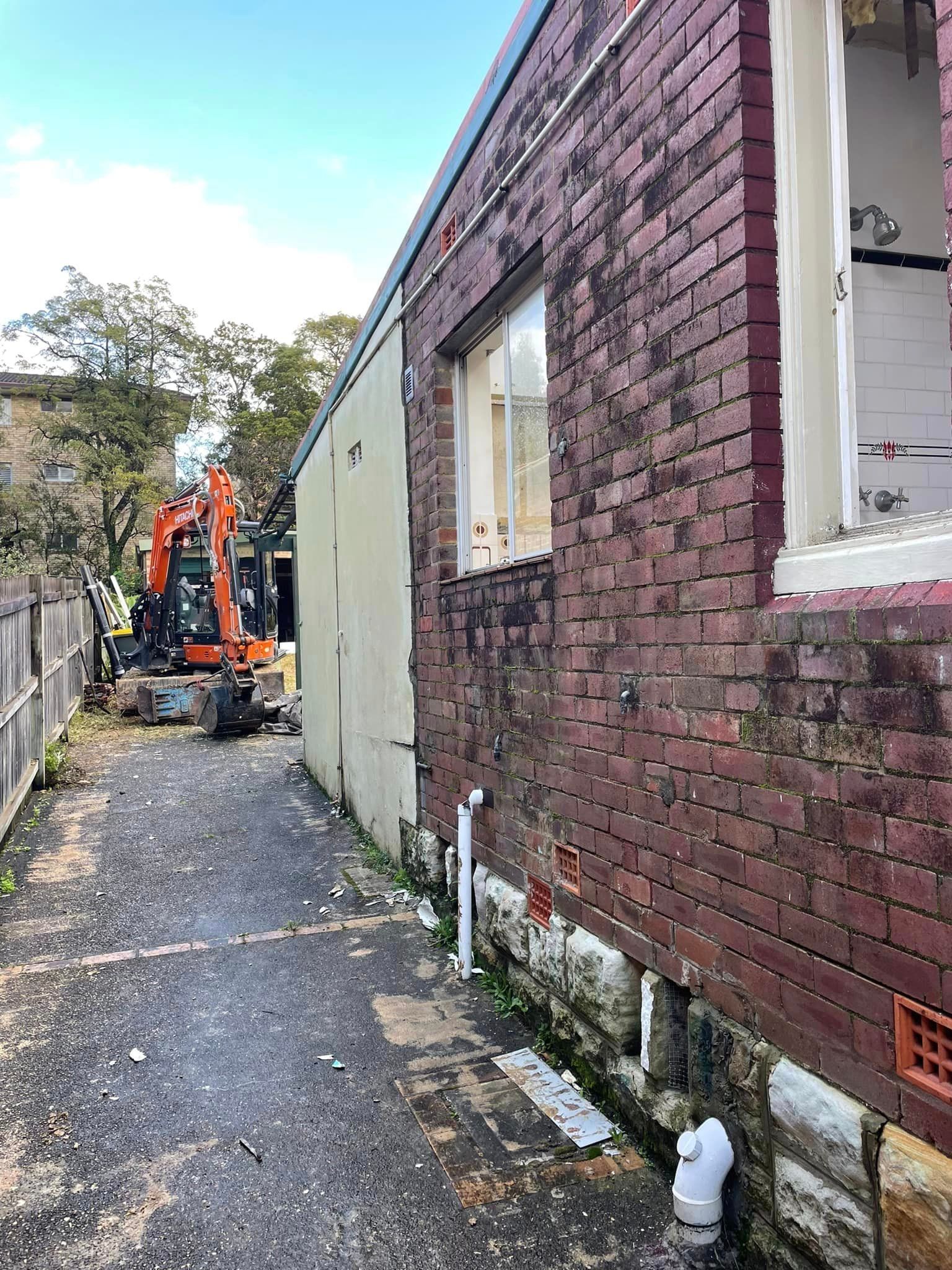 A brick building is being demolished with an excavator in the background.