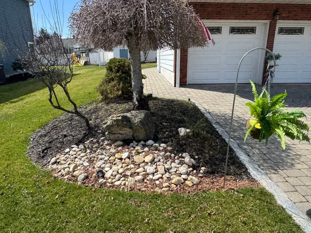 A garden with rocks and a tree in front of a garage.