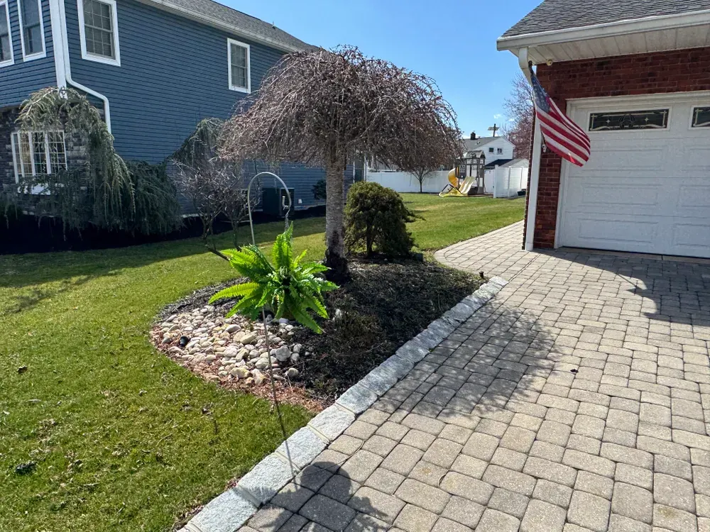 A brick driveway leading to a house with a garage and an american flag.