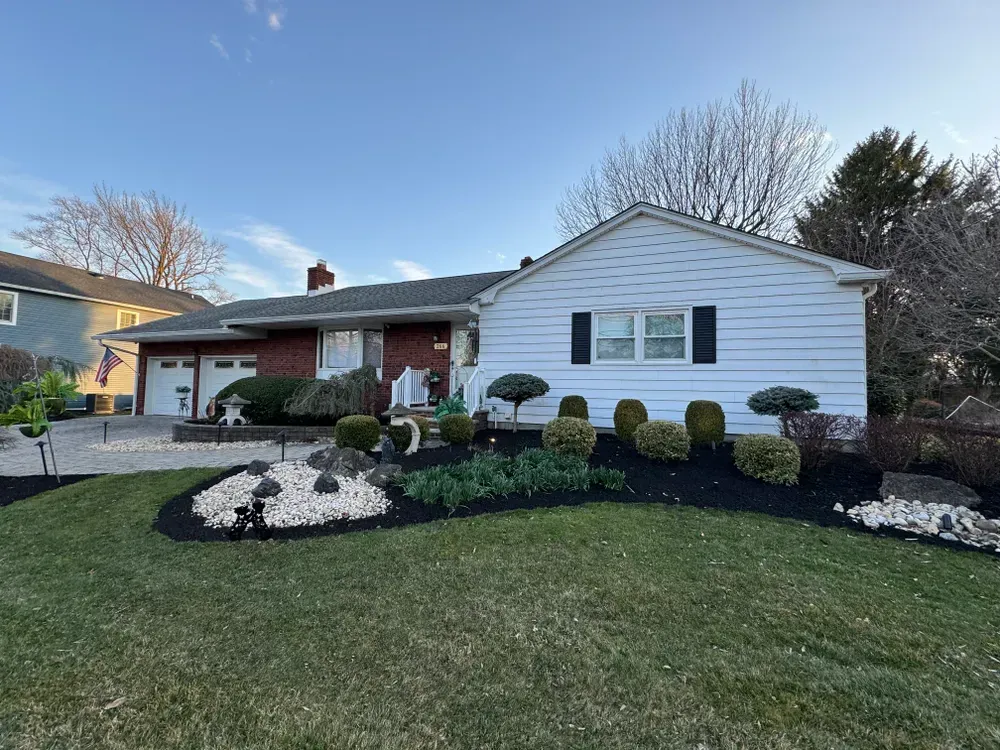 A white house with a brick roof and a large lawn in front of it.