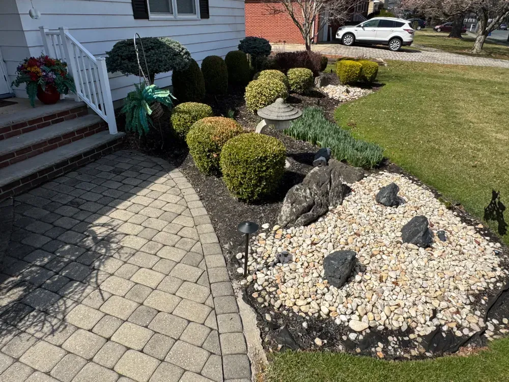 A brick walkway leading to a house with a rock garden in front of it.