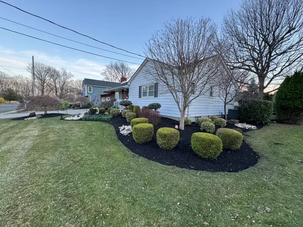 A white house with a lush green lawn and bushes in front of it.