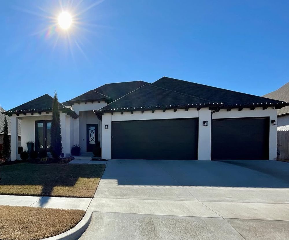 A white house with black garage doors and a blue sky in the background