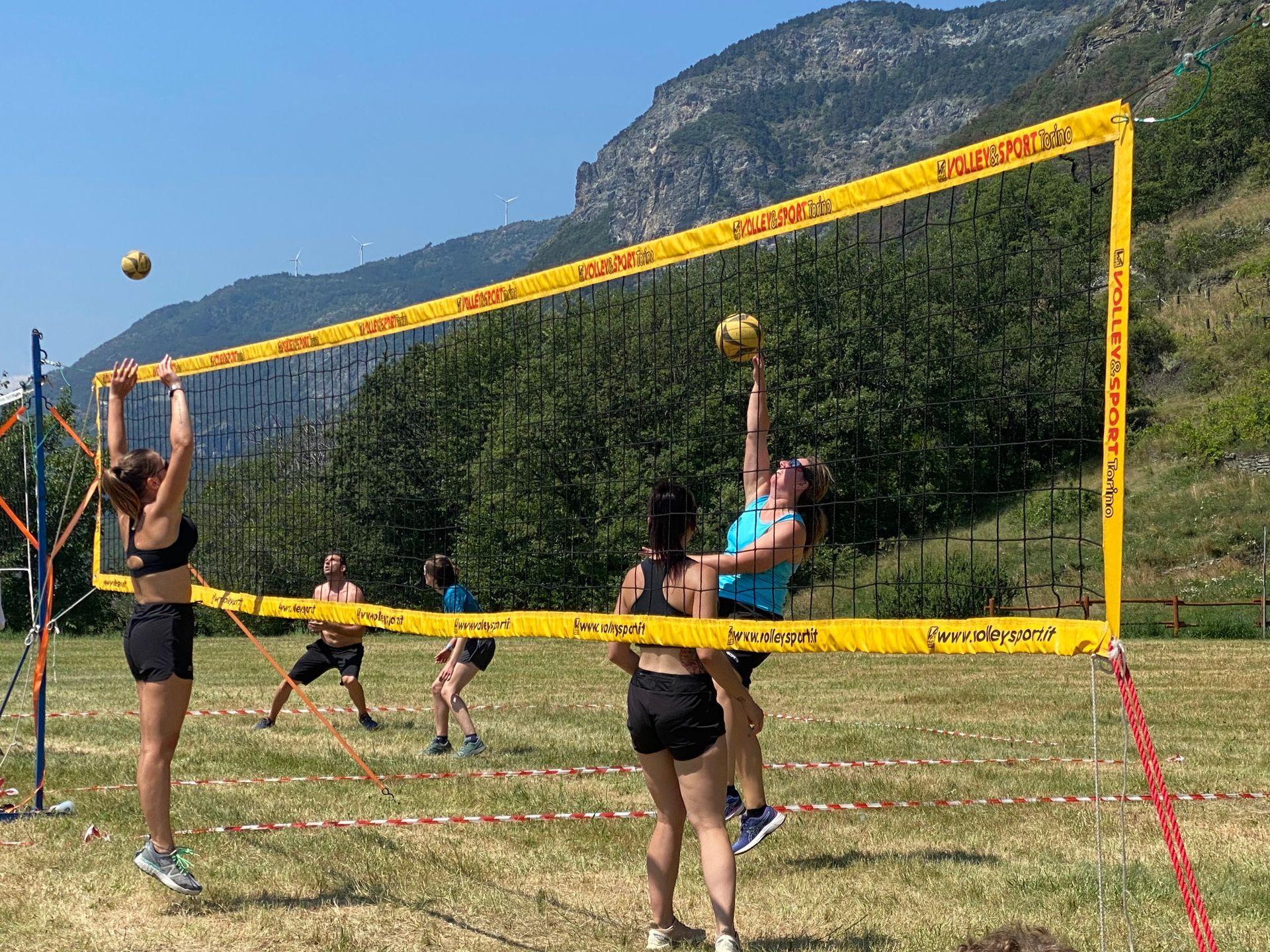 Partita del torneo di pallavolo su prato al Pekelin Strong Music Fest, con giocatori in azione sotto il sole estivo