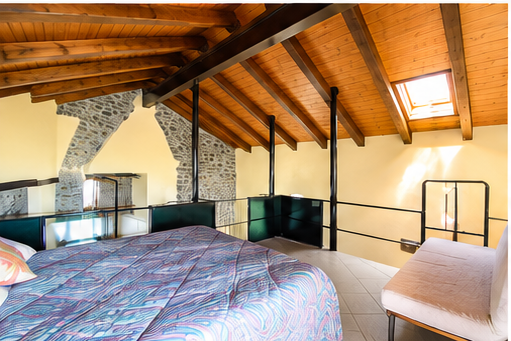 Zona notte su soppalco realizzata all'interno dell'antico fienile restaurato, con struttura in legno originale e atmosfera calda e accogliente.