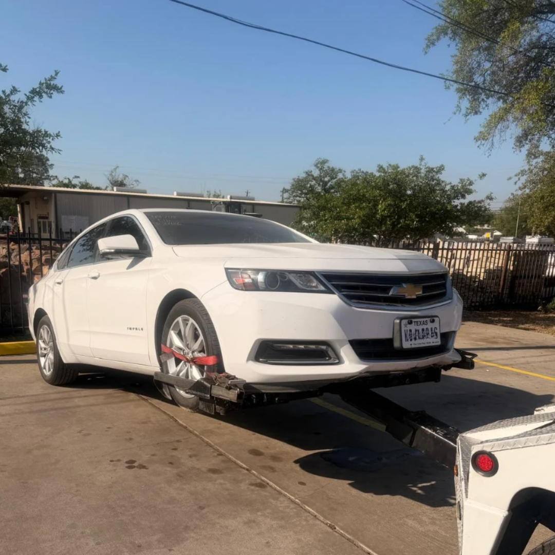 White sedan strapped on a tow truck in a sunny parking lot