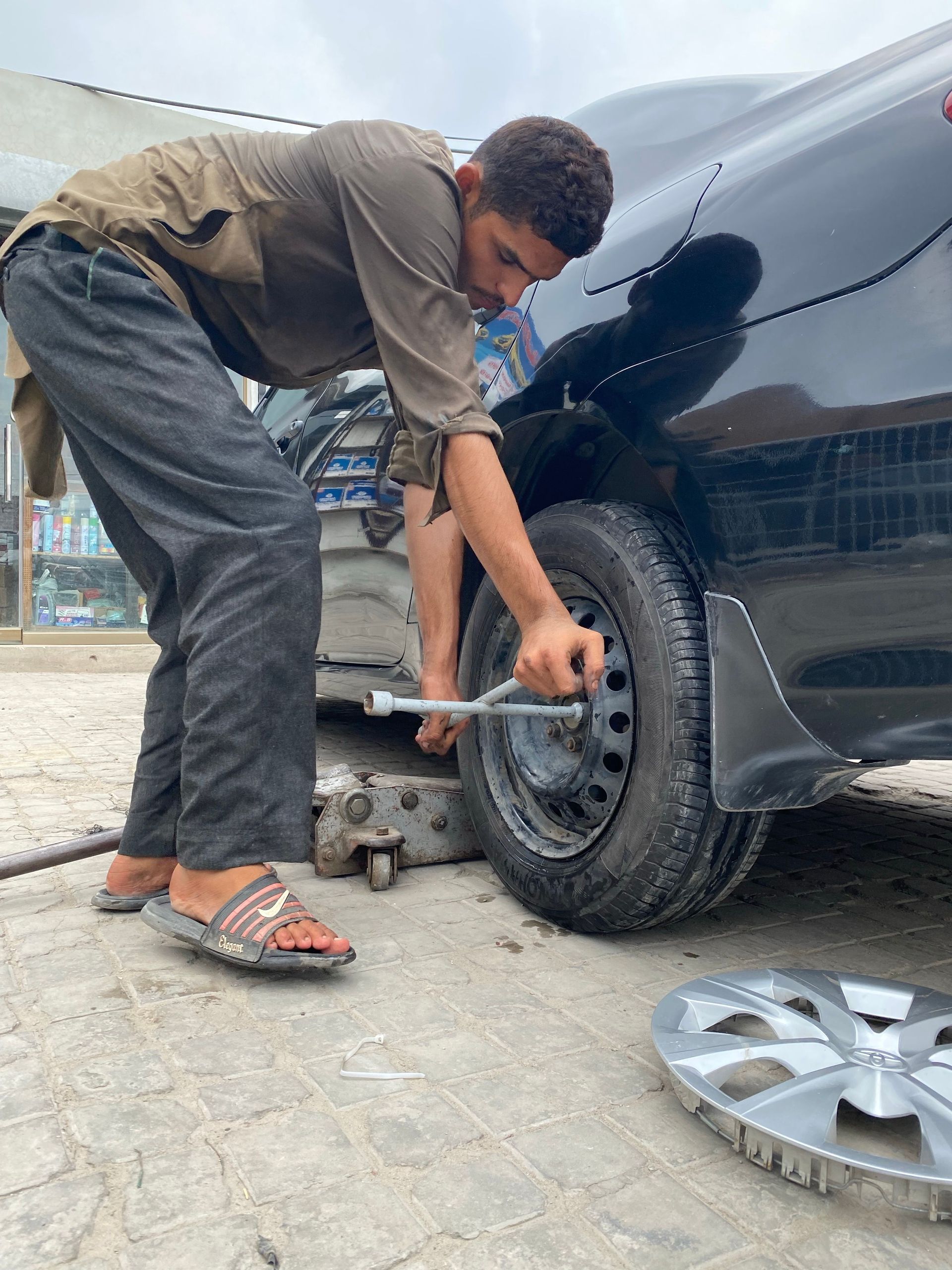 Person using a wrench to remove a car wheel beside a black vehicle in an outdoor repair area