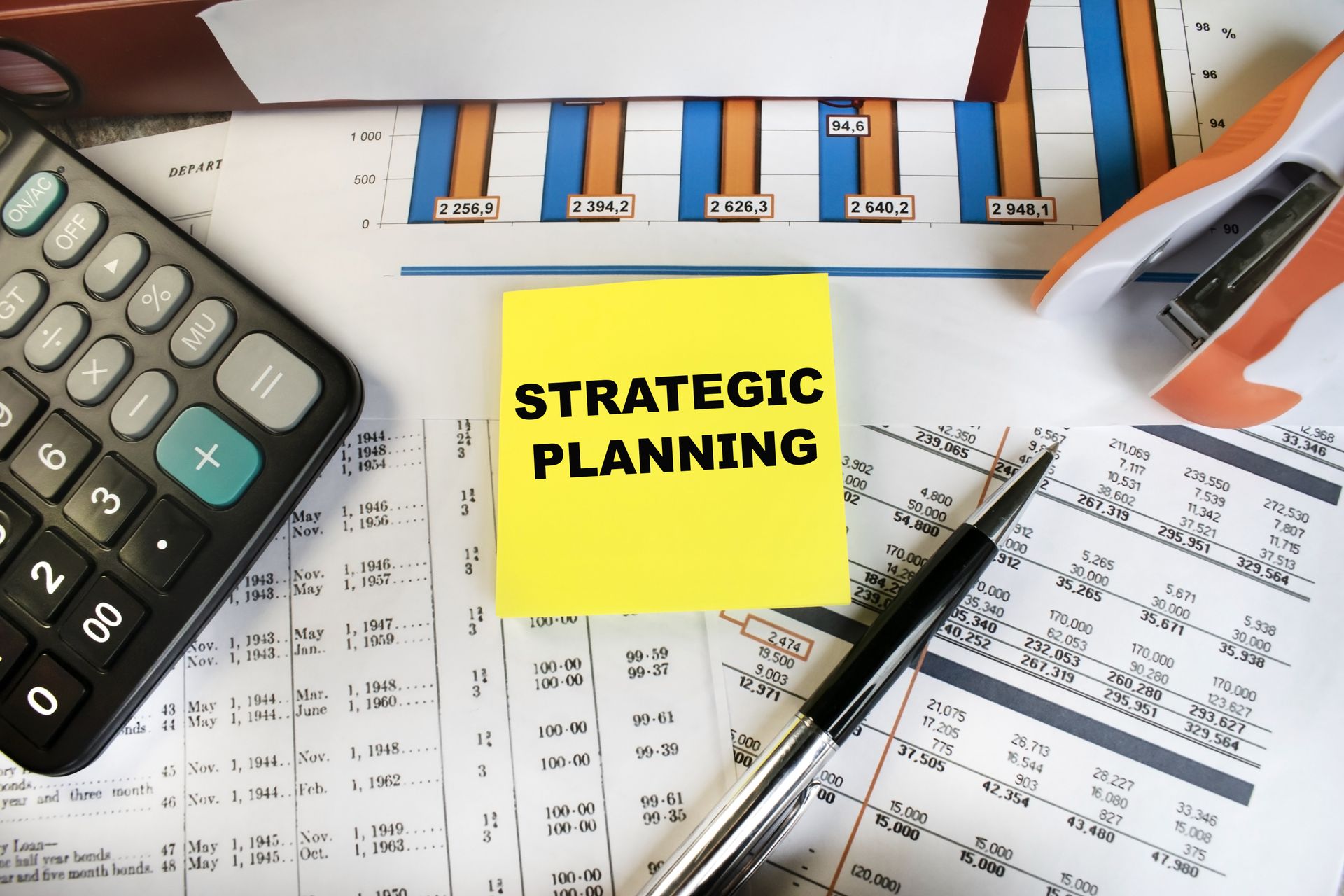 Strategic planning note on desk with calculator, pen, charts, and calendar pages