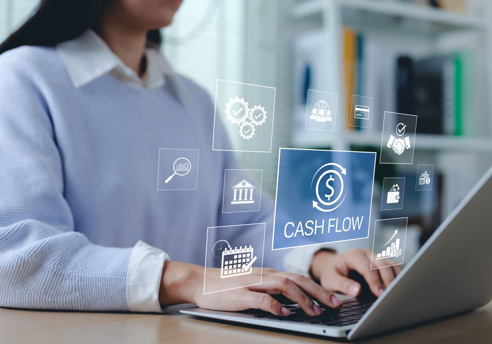 Person typing on a laptop with floating finance icons, including “cashflow,” in a bright office