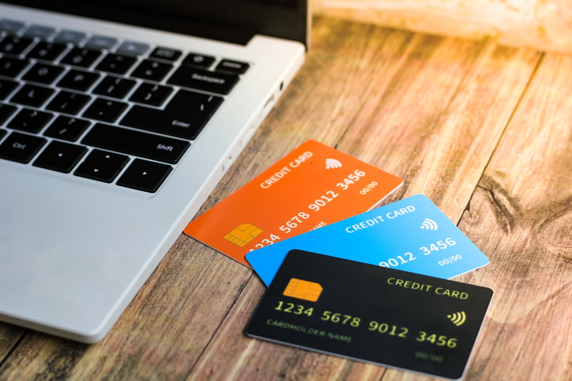 Laptop beside several colorful credit cards on a wooden desk