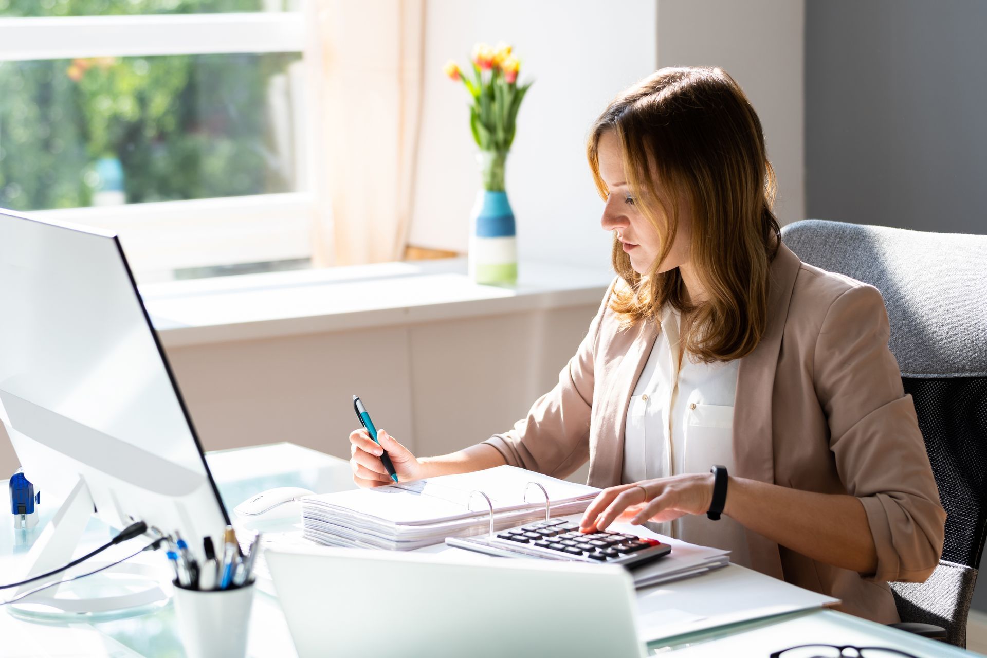 Woman working at a desk with papers and a laptop in a bright office by a window