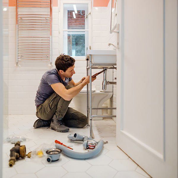 Plumber Fixing a Leak Under the Bathroom Sink — Plainview, NY — Martino Plumbing & Heating INC. Plumber Fixing a Leak Under the Bathroom Sink — Plainview, NY — Martino Plumbing & Heating INC.