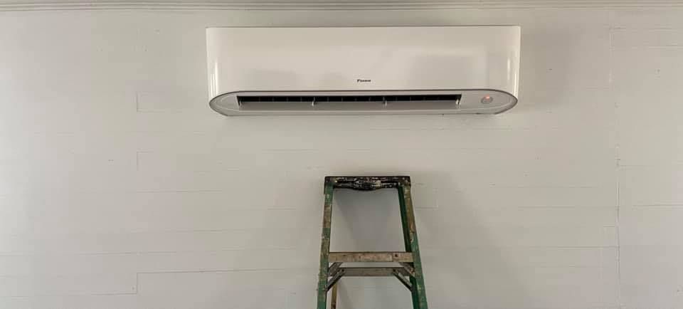 White wall-mounted air conditioner above a step ladder against a white wall.