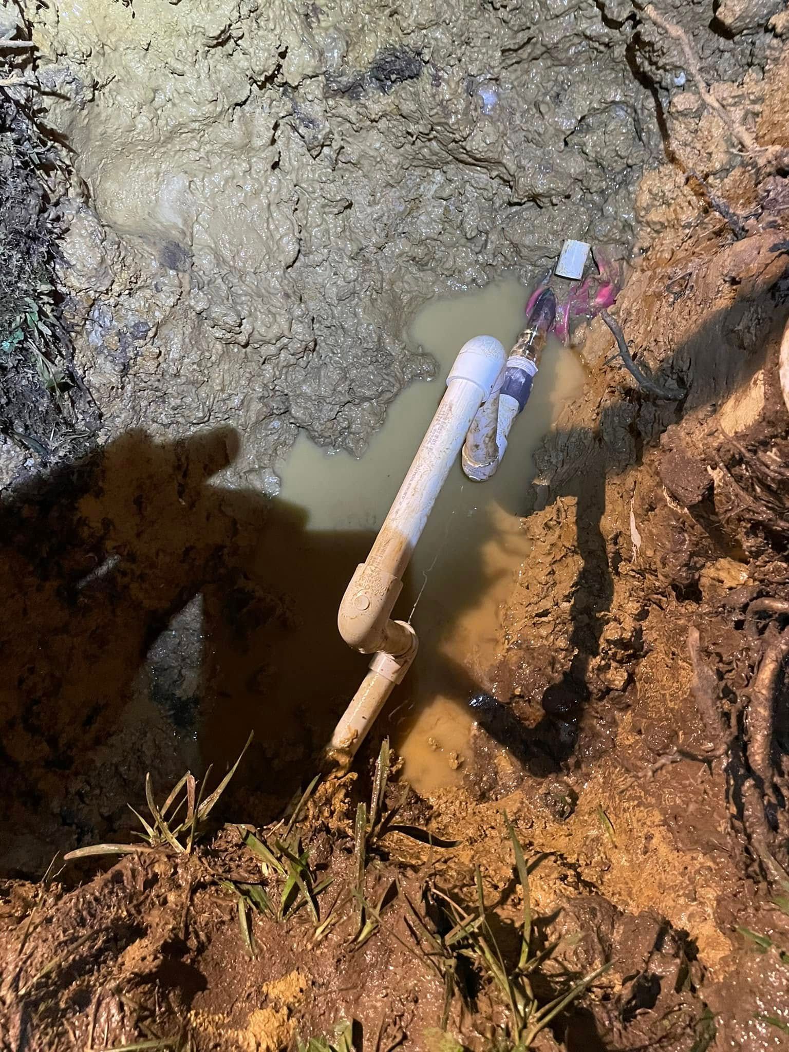 A flooded excavation pit with PVC pipes, dirt, and muddy water.