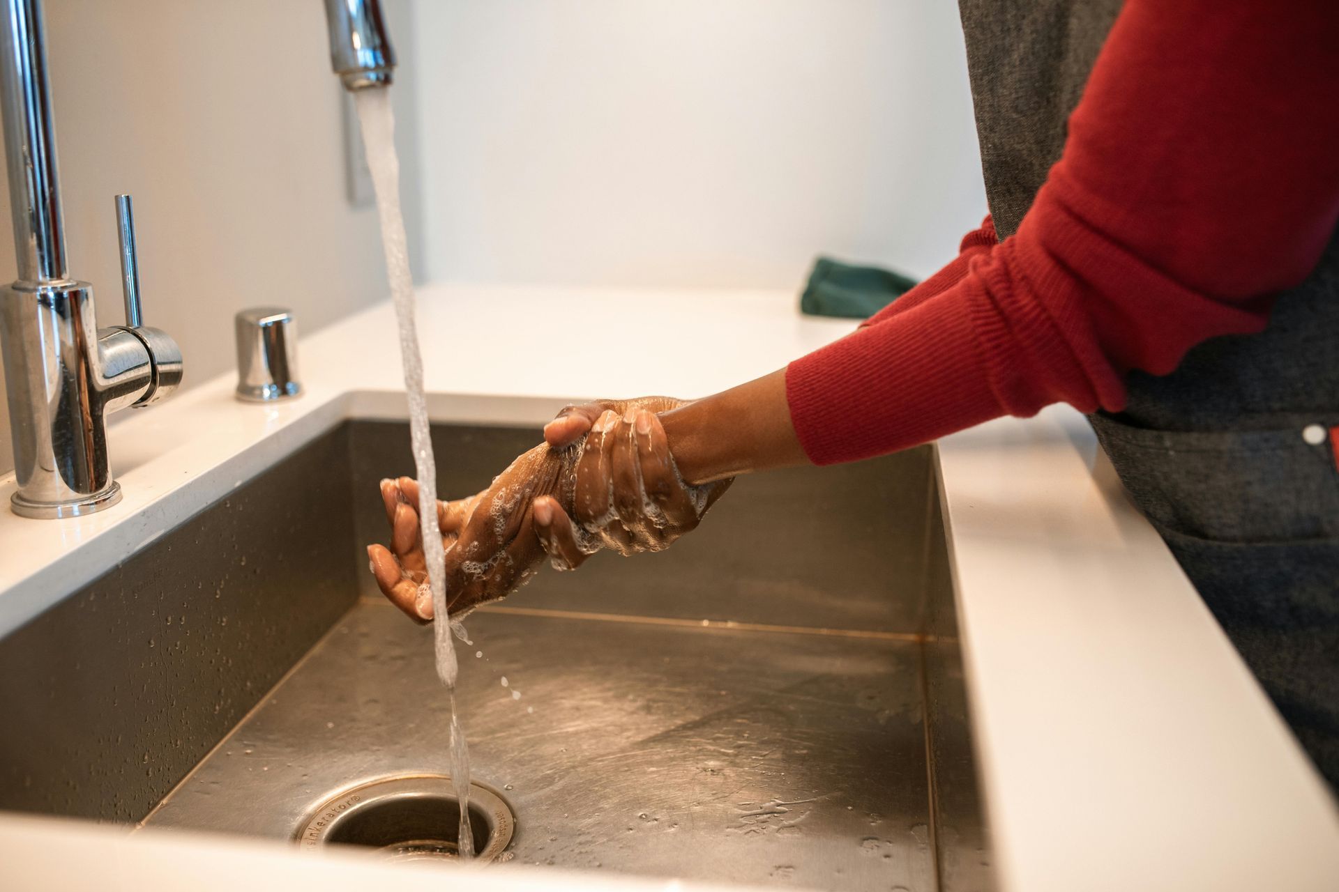 Person washing hands with running water in a stainless steel sink.