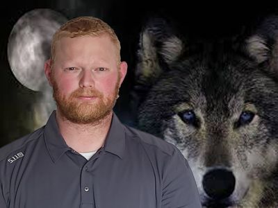 A man with a beard is standing in front of a wolf.