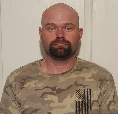 A bald man with a beard is wearing a camouflage shirt.