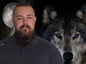 A man with a beard is standing in front of a wolf.