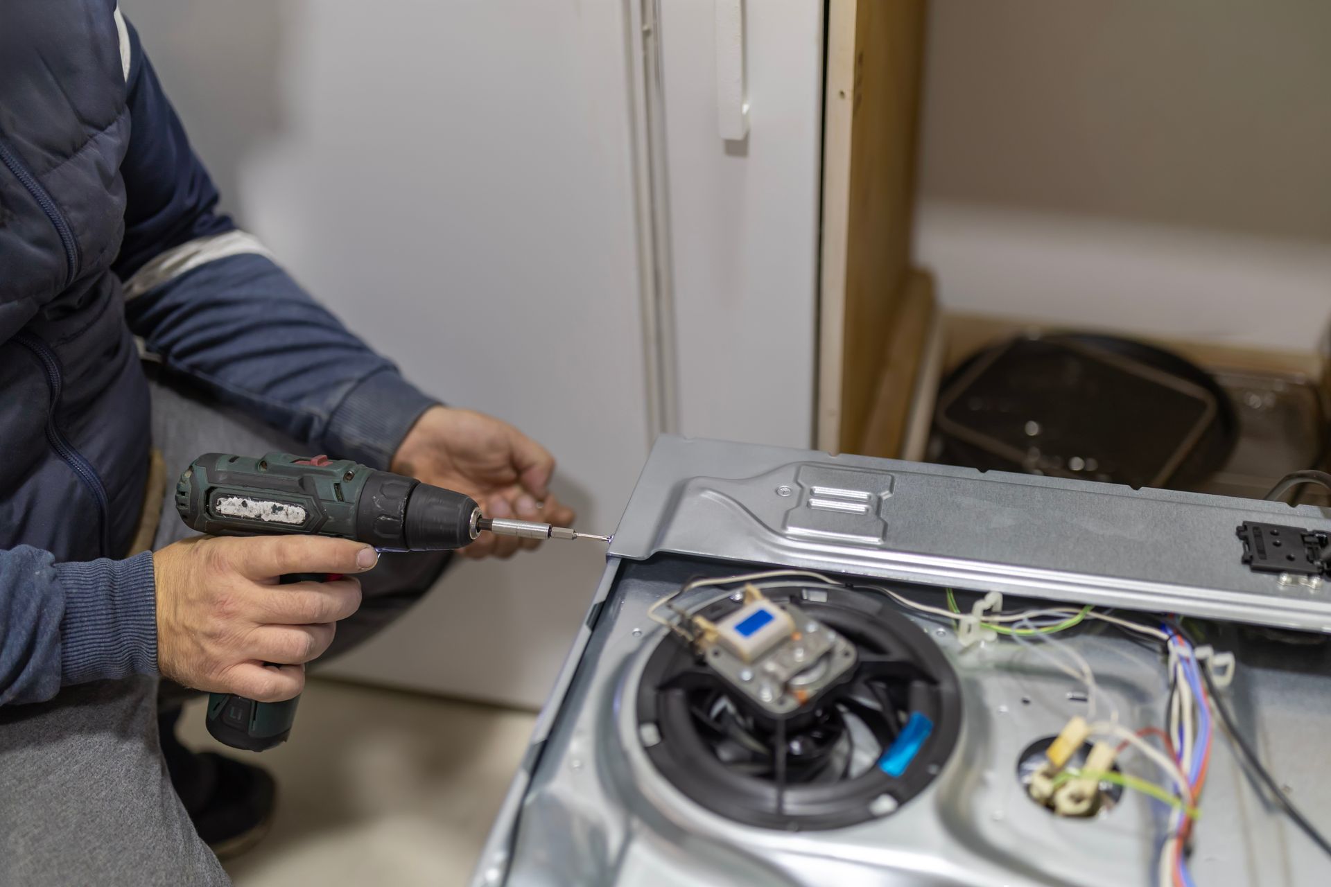 Person using a power drill to assemble or repair appliance component.