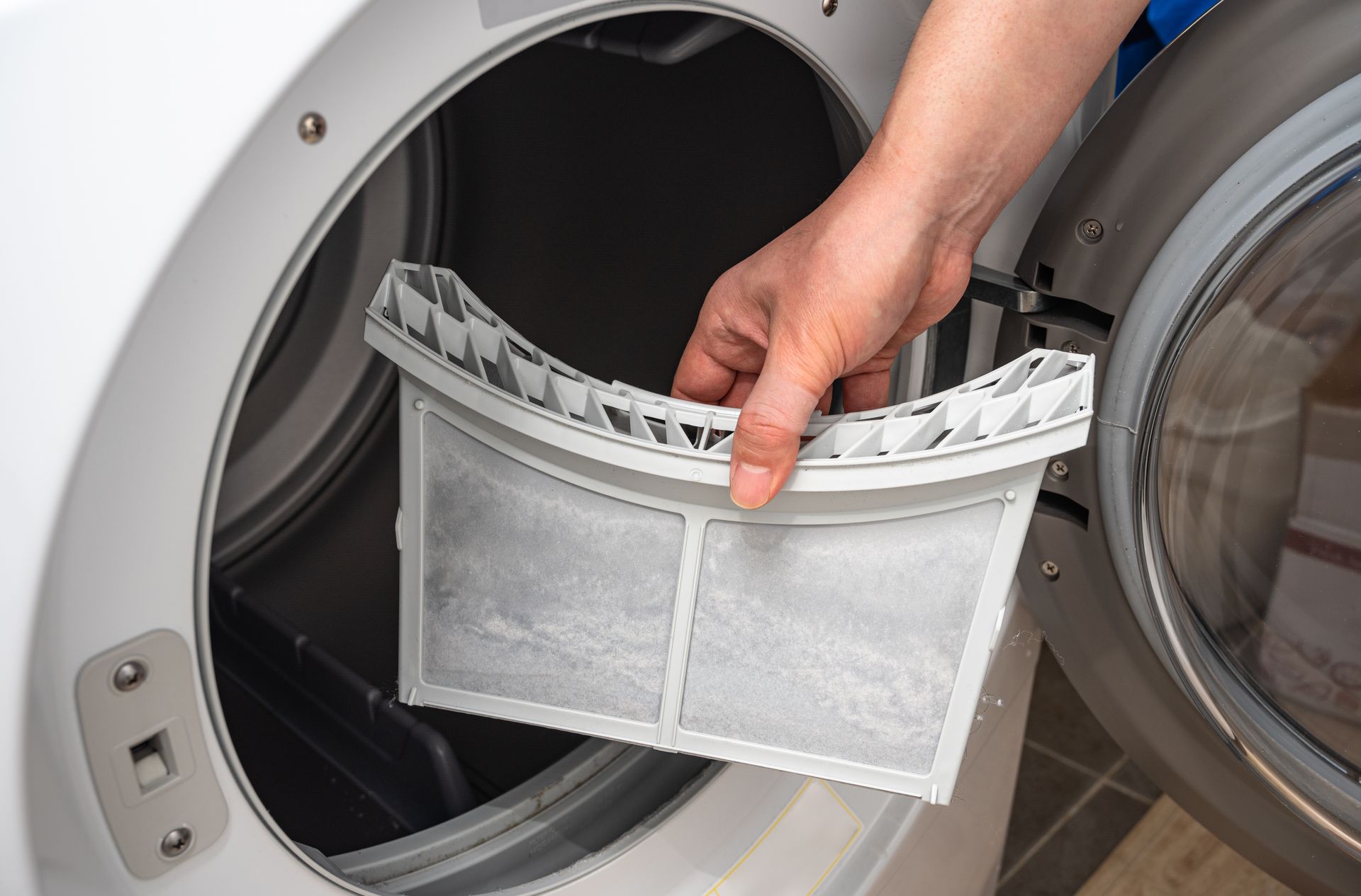 A person repairs a washing machine, using a screwdriver, with the door open.