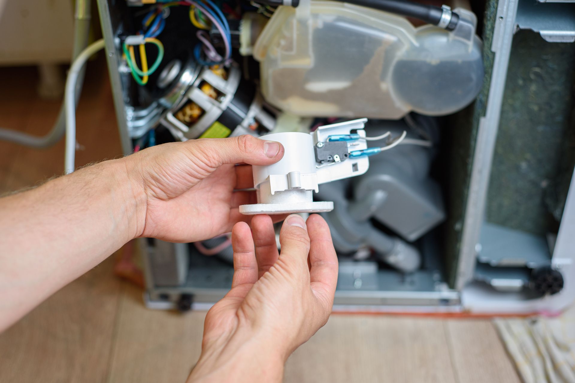 Person repairing a dishwasher, holding a white component. Interior shot, tools visible.