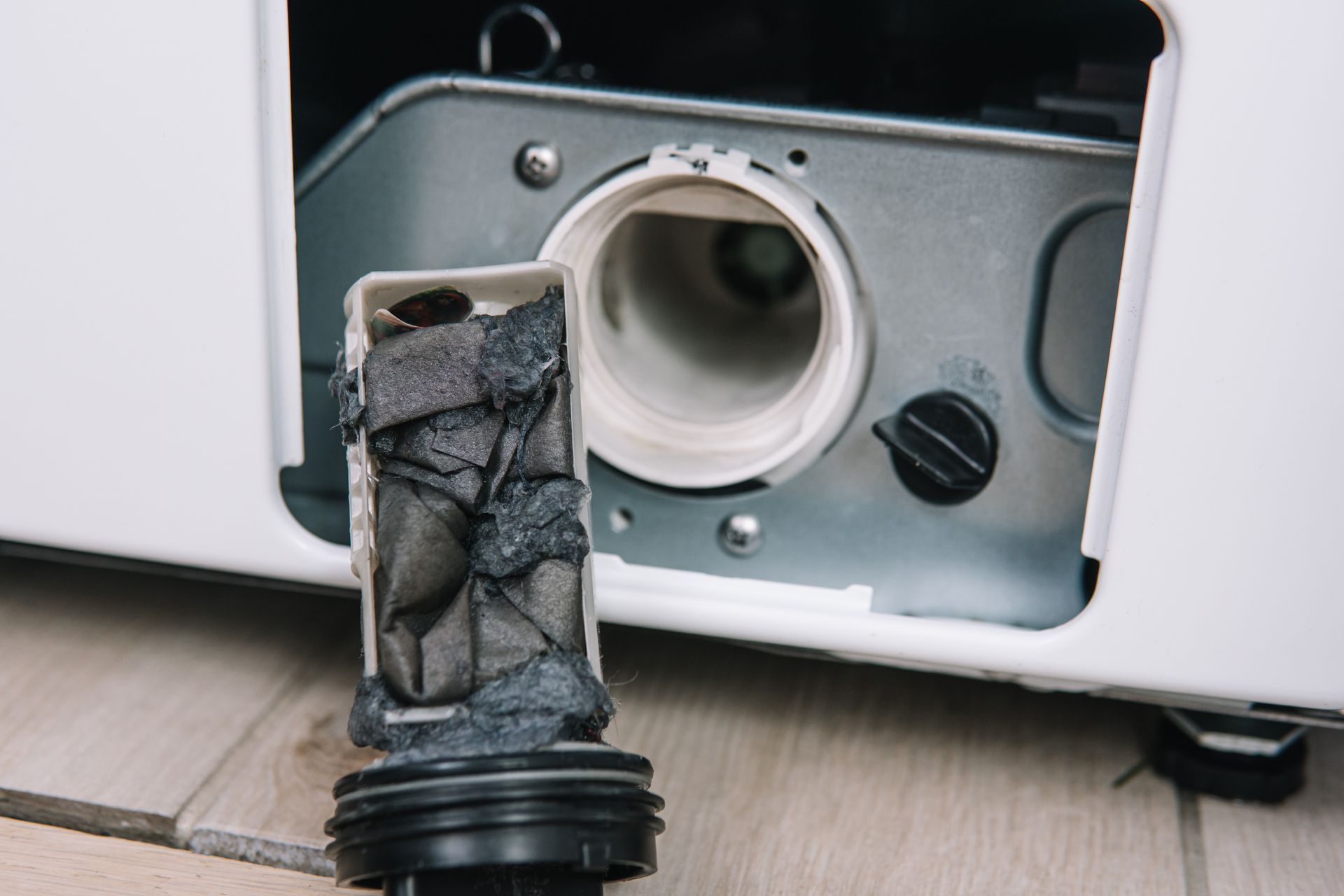 Washing machine lint filter removed, showing thick buildup. White machine, gray filter, black cap.