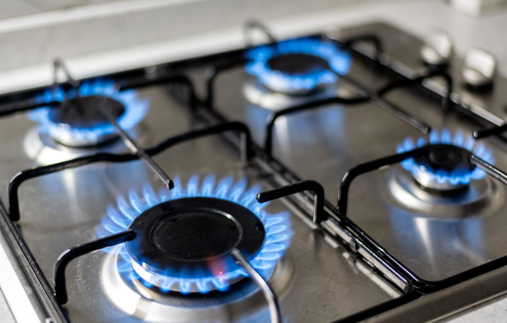 Gas stovetop with four blue flames burning brightly.