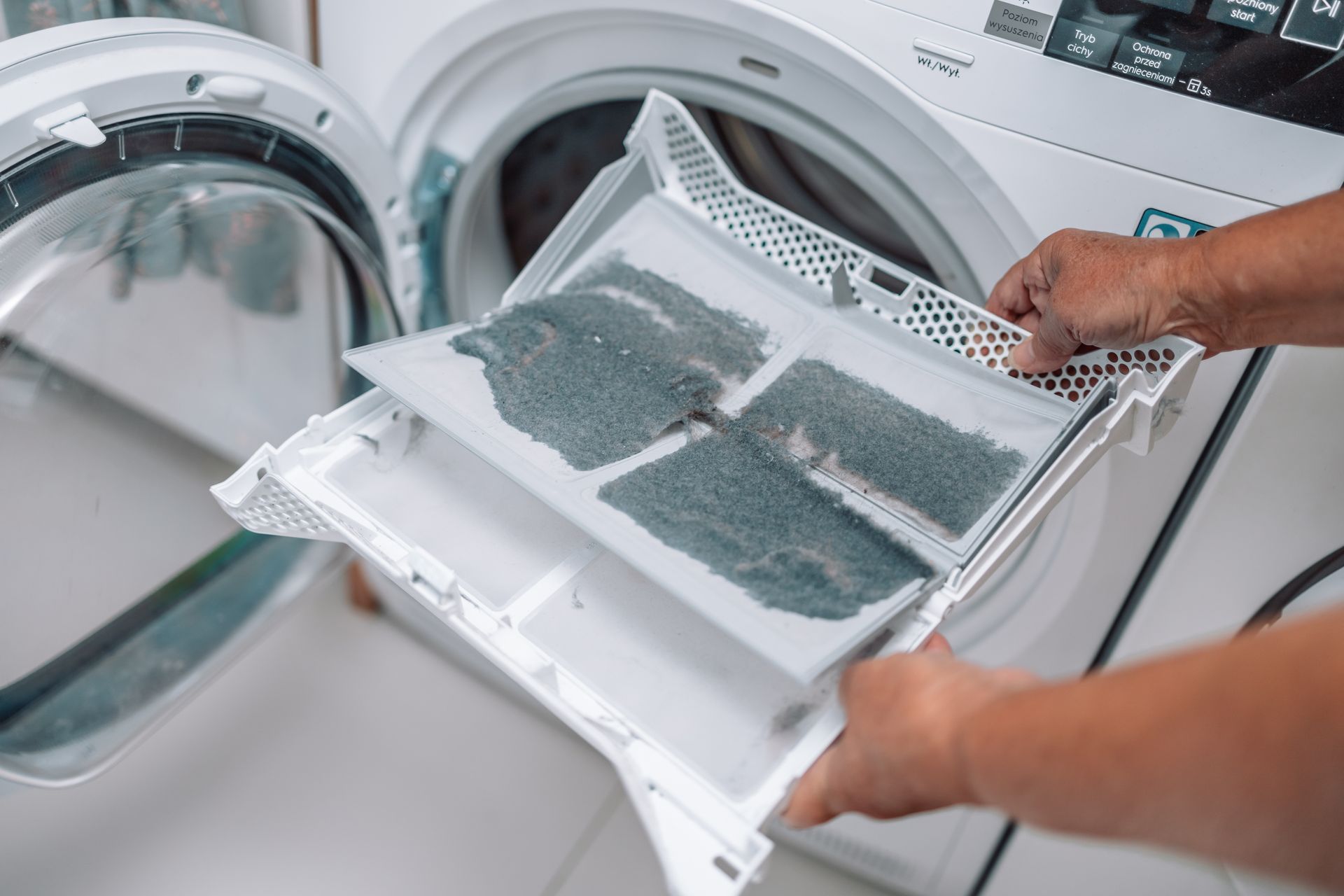 Person holding a lint filter from a dryer, showing a buildup of gray lint.