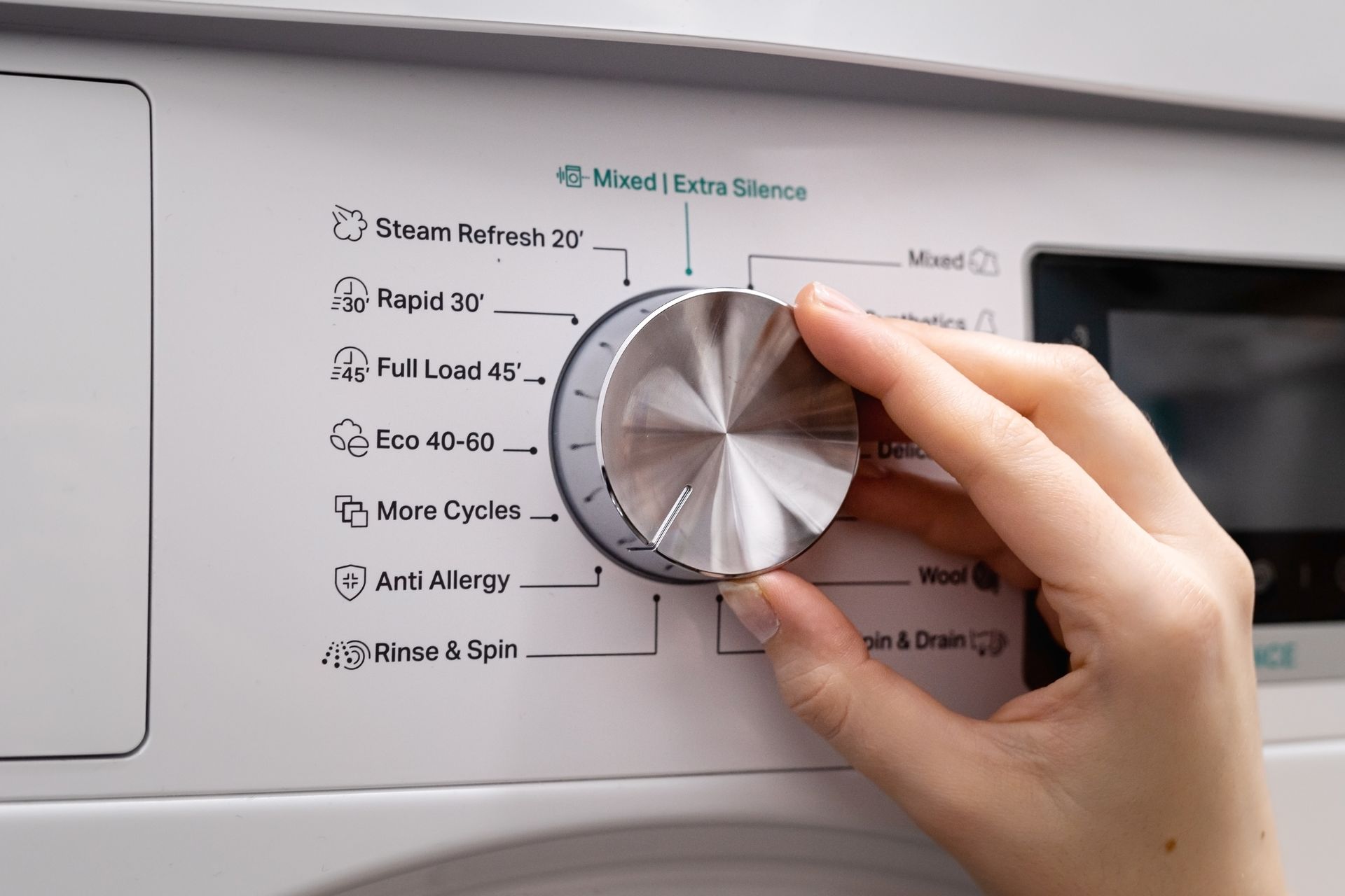 Hand turning a dial on a white washing machine, selecting a wash cycle.