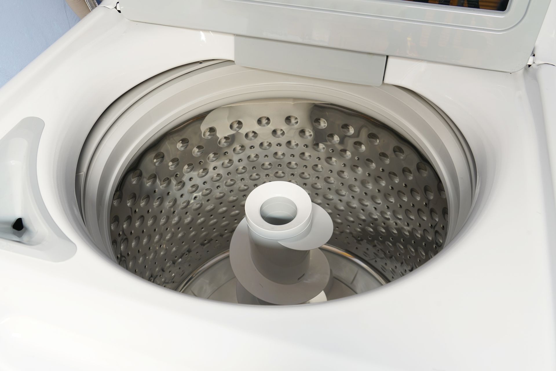 Person repairs a washing machine, using a screwdriver. White appliance, exposed internal parts, tools on the floor.