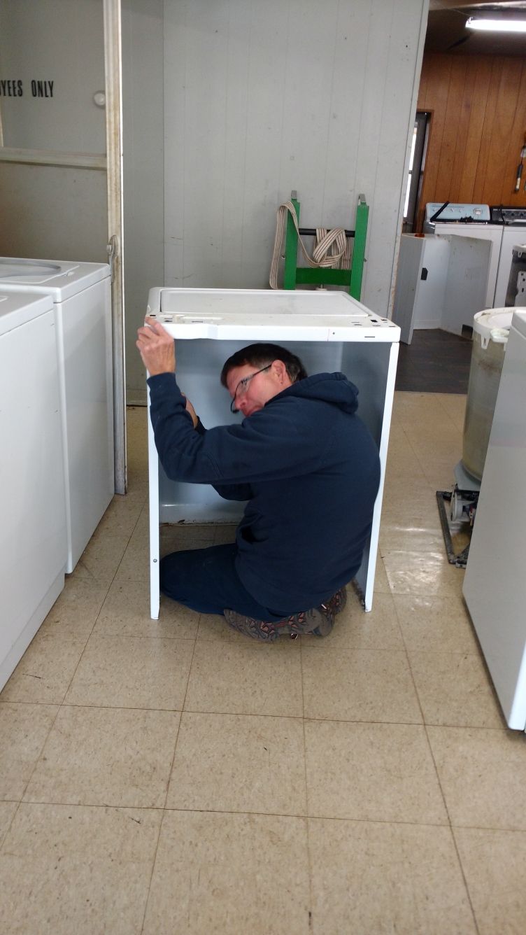 Man repairing dryer, kneeling on floor, working on internal components.